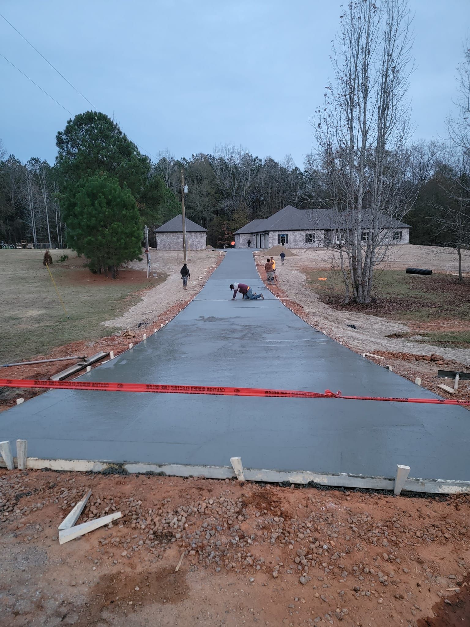 Concrete driveway under construction; workers finishing the pour on a cloudy day.