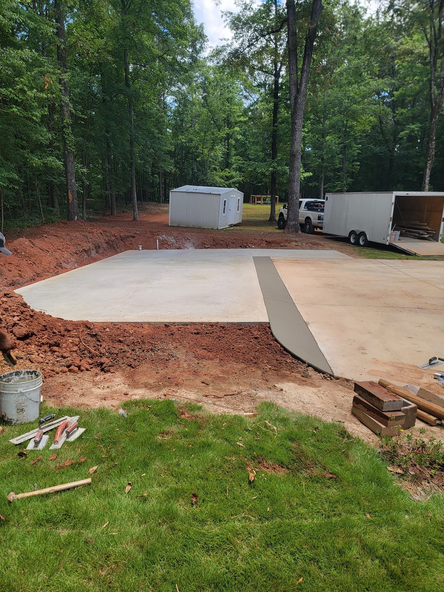 Concrete pad construction site with dirt, grass, trees, and trailers.