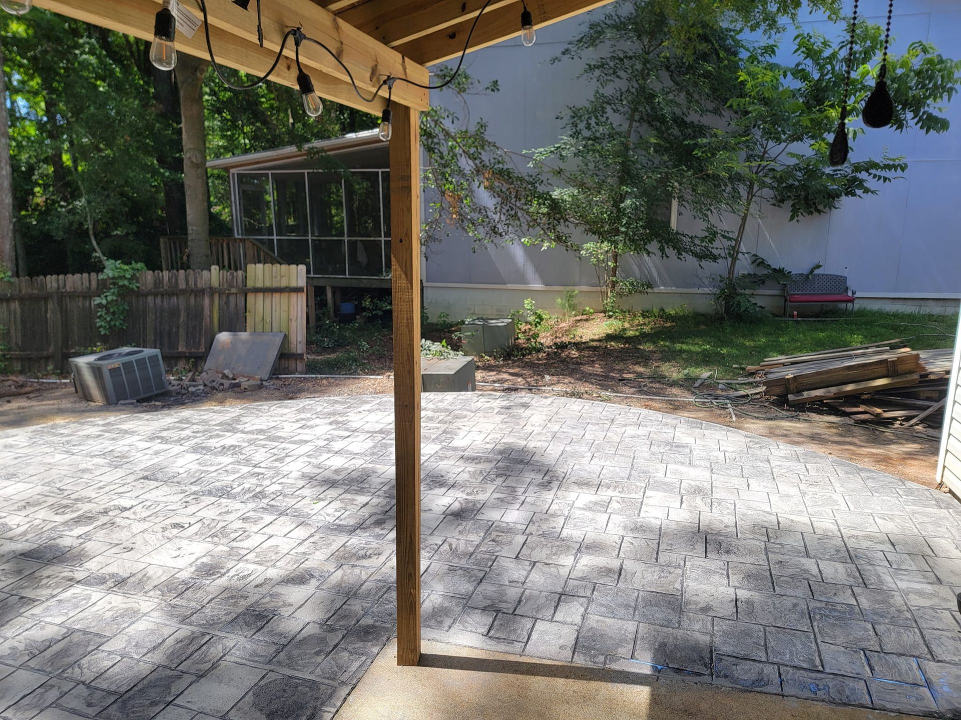 Patio with paved stones, wooden post, and a view of yard with trees and a screen enclosure.