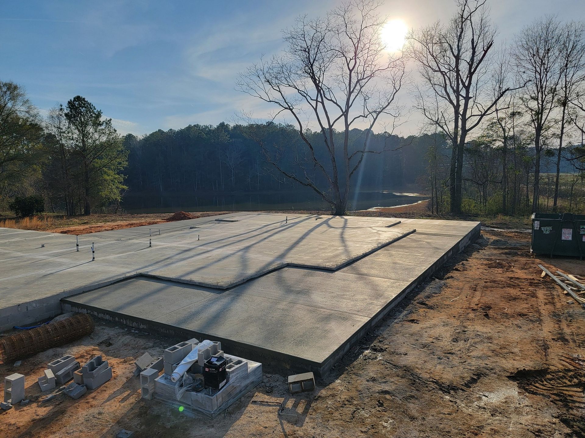 Concrete foundation on a cleared lot with trees in the background under a sunny sky.