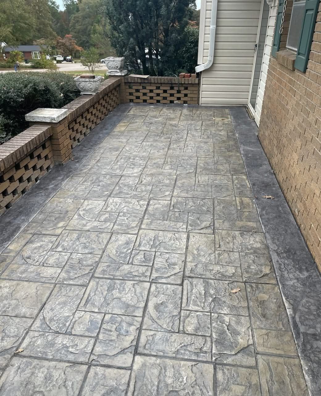 A gray, stamped concrete patio with a brick wall and the side of a house.