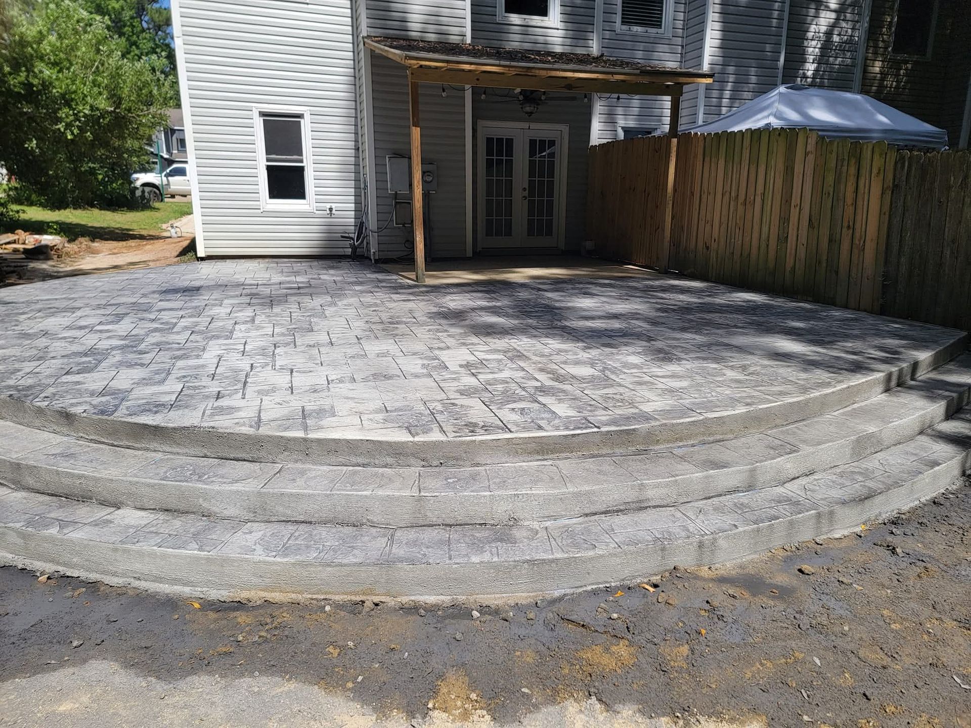 A gray stone patio with curved steps leading up to a house with a wooden pergola.