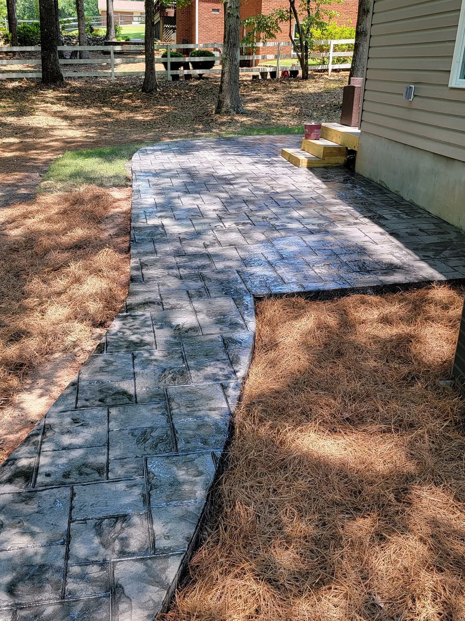 Brick walkway next to a building, bordered by brown mulch, in an outdoor setting.