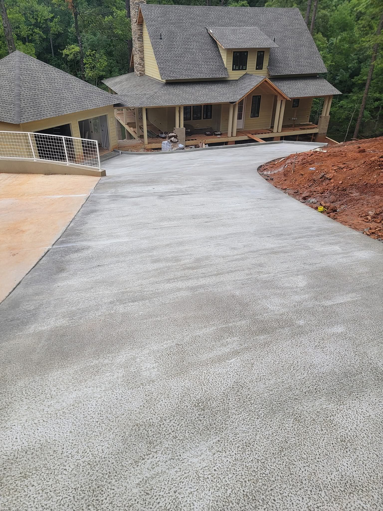 New concrete driveway leading to a light-yellow house with a wooden porch and brown roof.