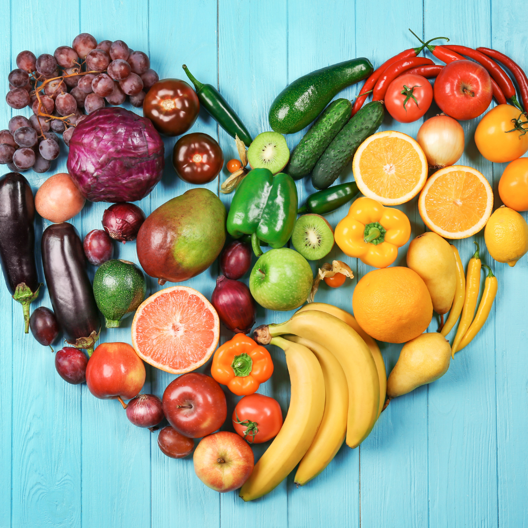 Heart shape formed with colorful fruits and vegetables on a blue wooden surface.