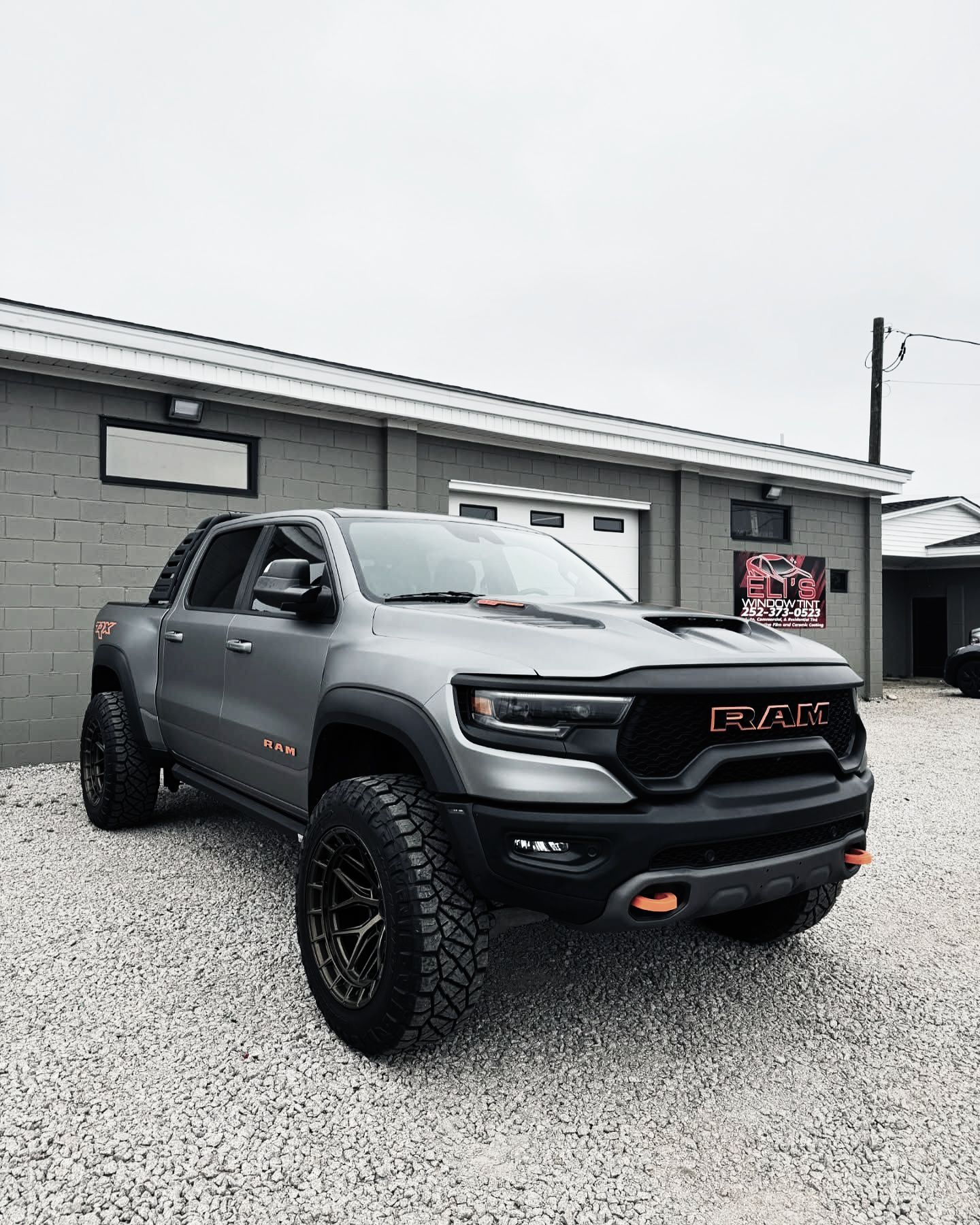Gray Ram TRX truck parked in front of a gray building on gravel.