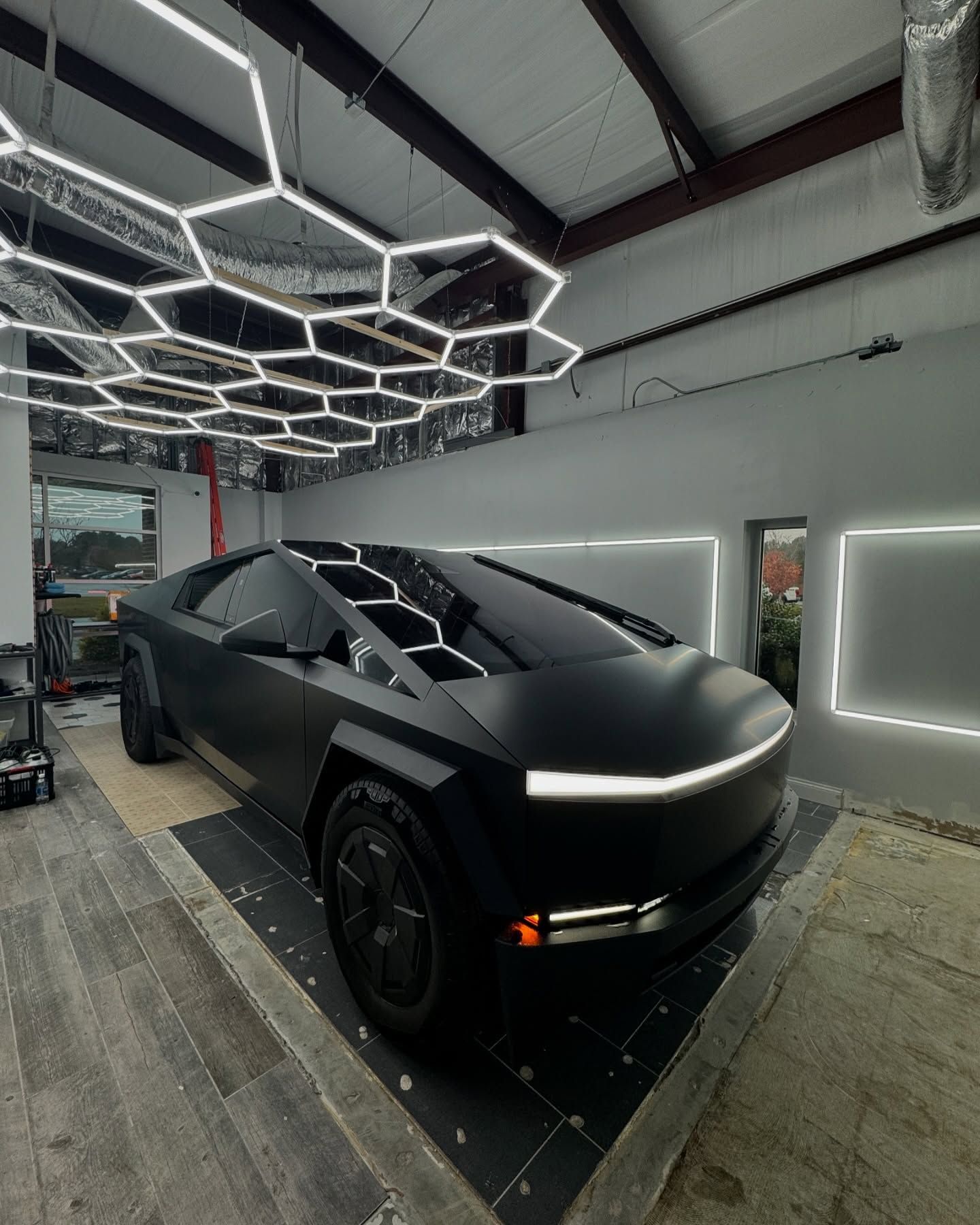 Black Tesla Cybertruck in a well-lit garage, with geometric lights overhead.