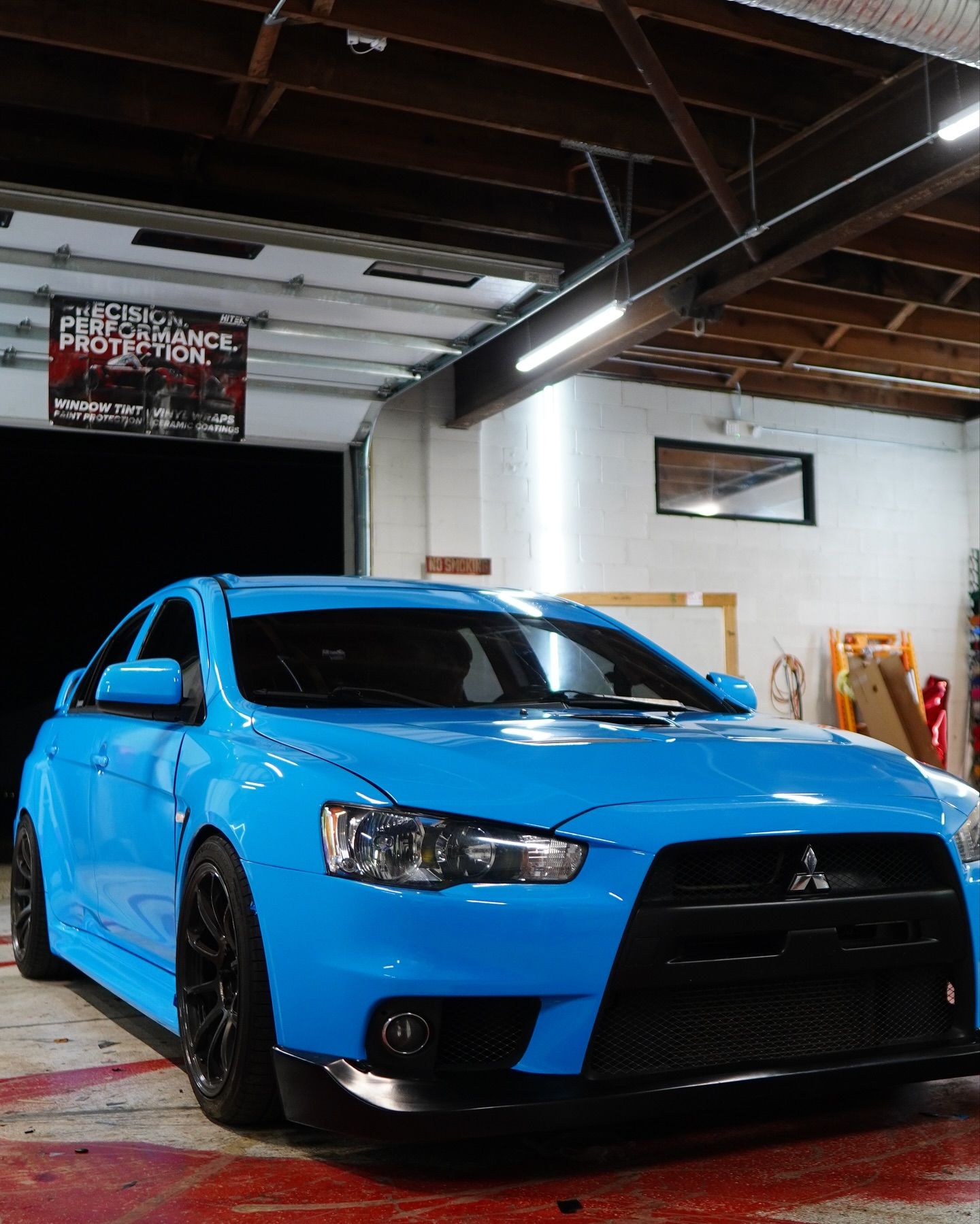 Bright blue Mitsubishi Lancer Evolution with black accents parked inside a garage.