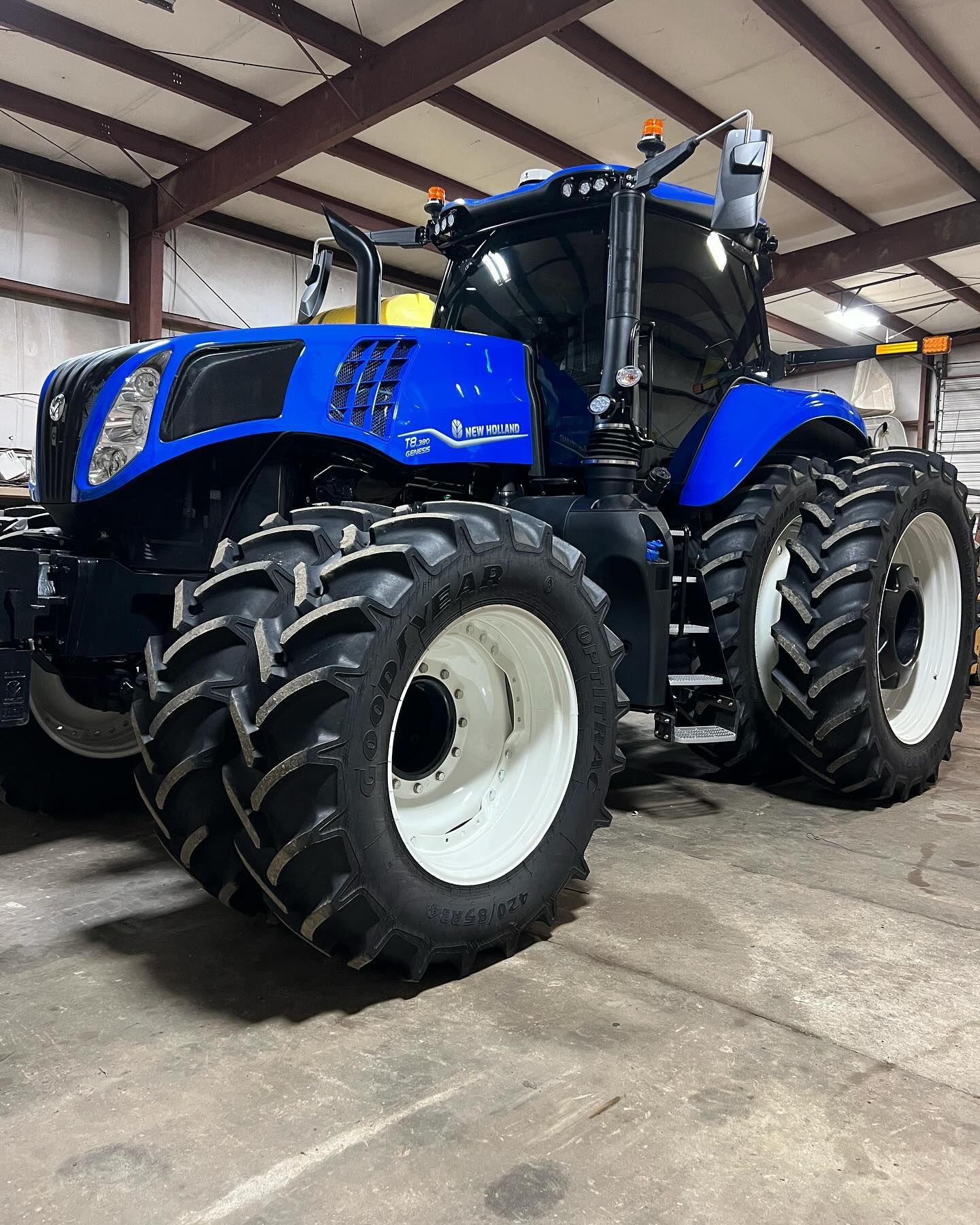 Blue New Holland tractor with white wheels, parked inside a building with a corrugated metal ceiling.