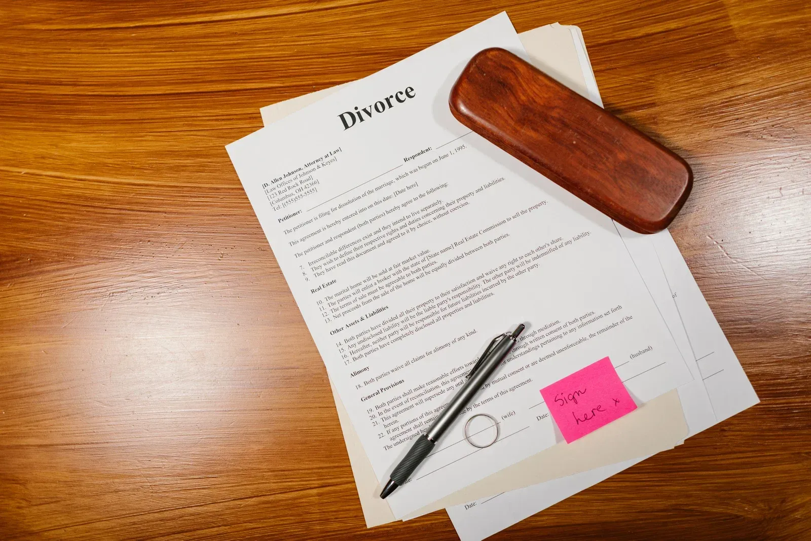 Divorce papers, pen, eyeglasses case, and sticky note on a wooden table.