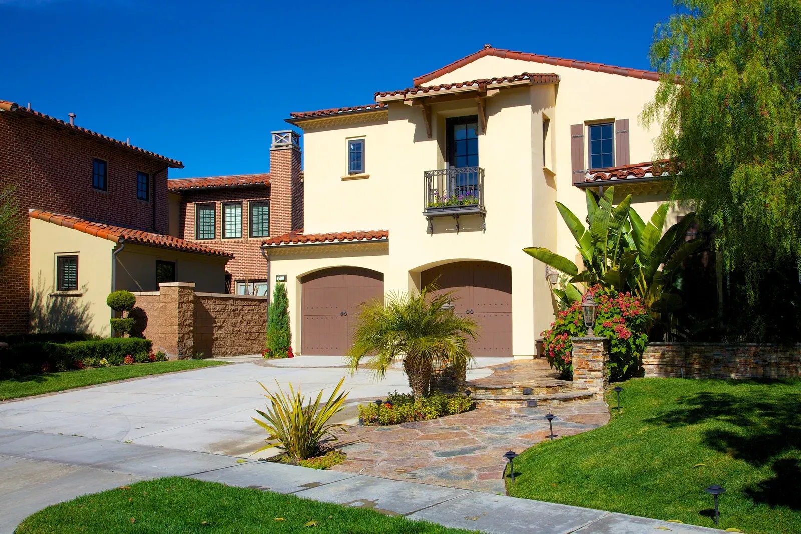 Beige stucco house with brown garage doors, red tile roof, and green lawn.