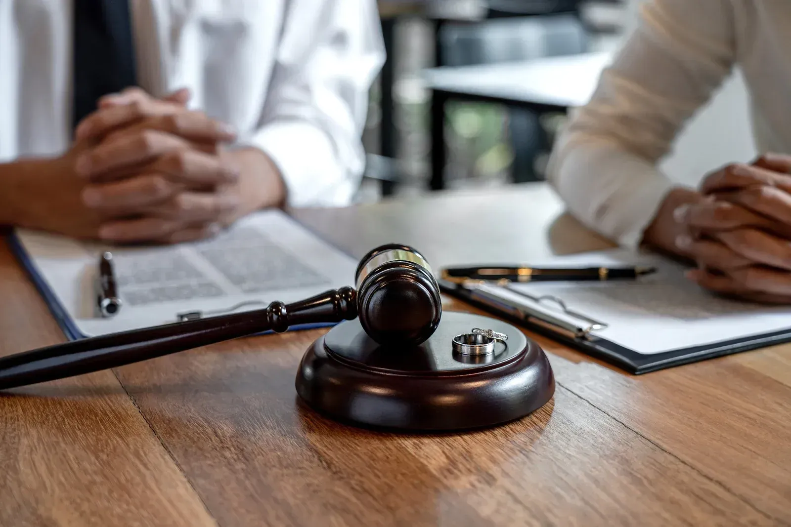 Gavel on wooden table with documents and hands in a legal setting.