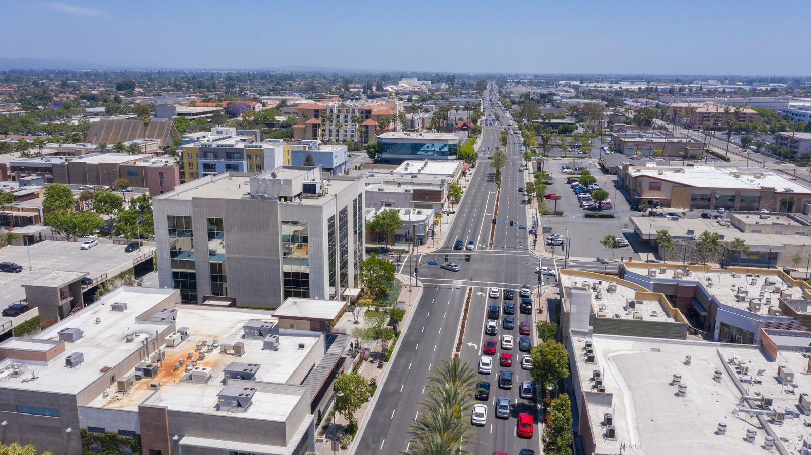 Aerial view of a city street with traffic and buildings under a bright blue sky.