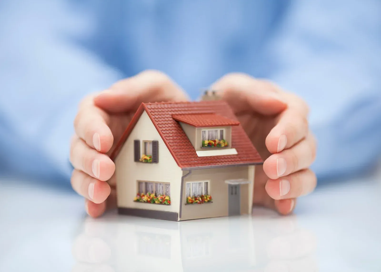 Hands cupping a miniature house with a red roof, suggesting protection or homeownership.