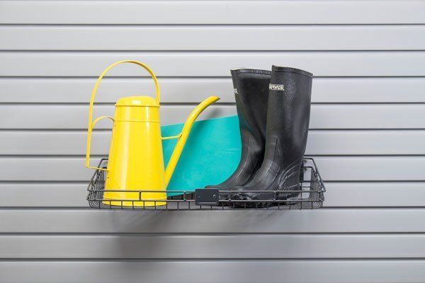 A pair of black boots and a yellow watering can are sitting on a shelf.