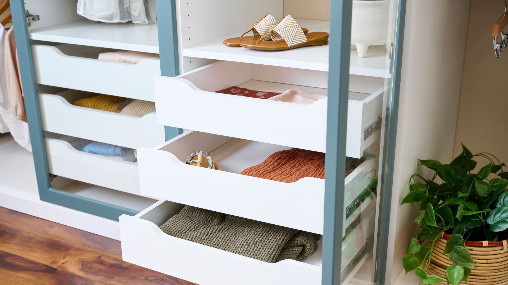 White closet with built-in drawers holding folded clothes. A pair of sandals sits on a shelf above.