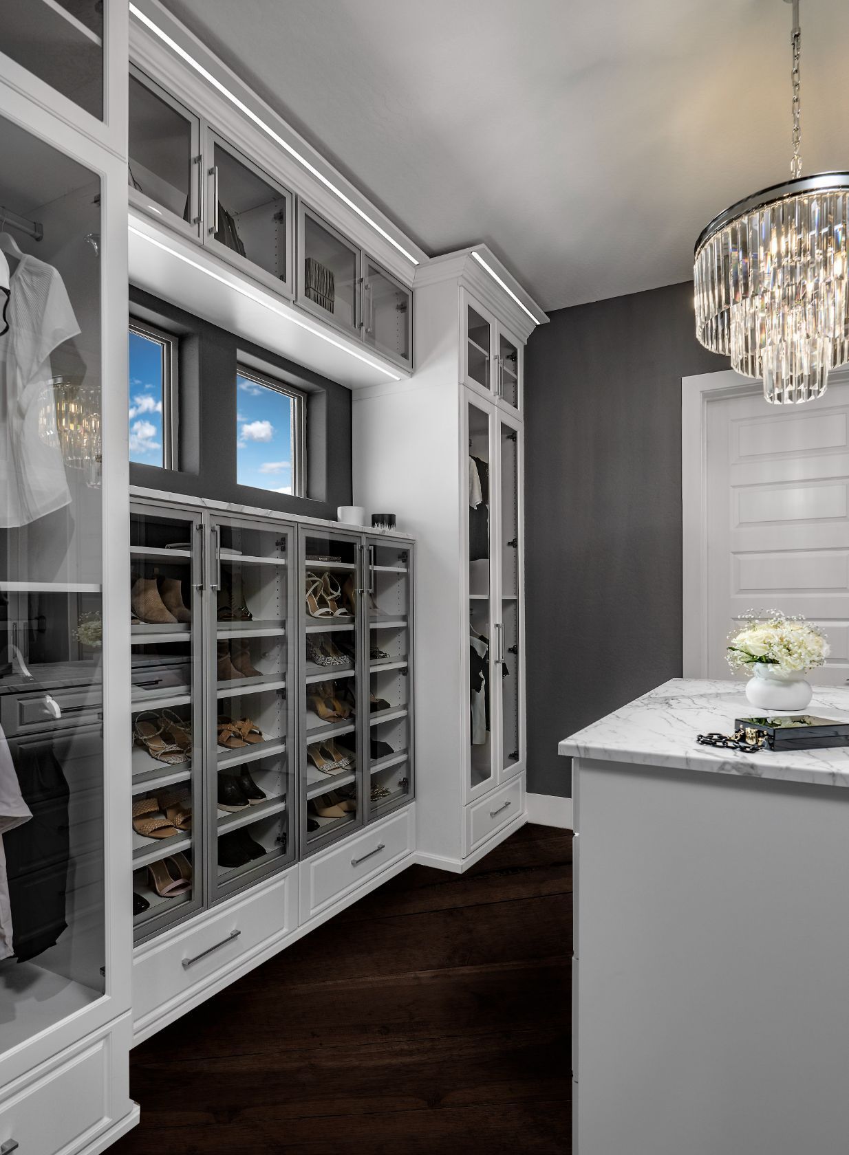 A walk in closet with lots of shelves and drawers and a chandelier.