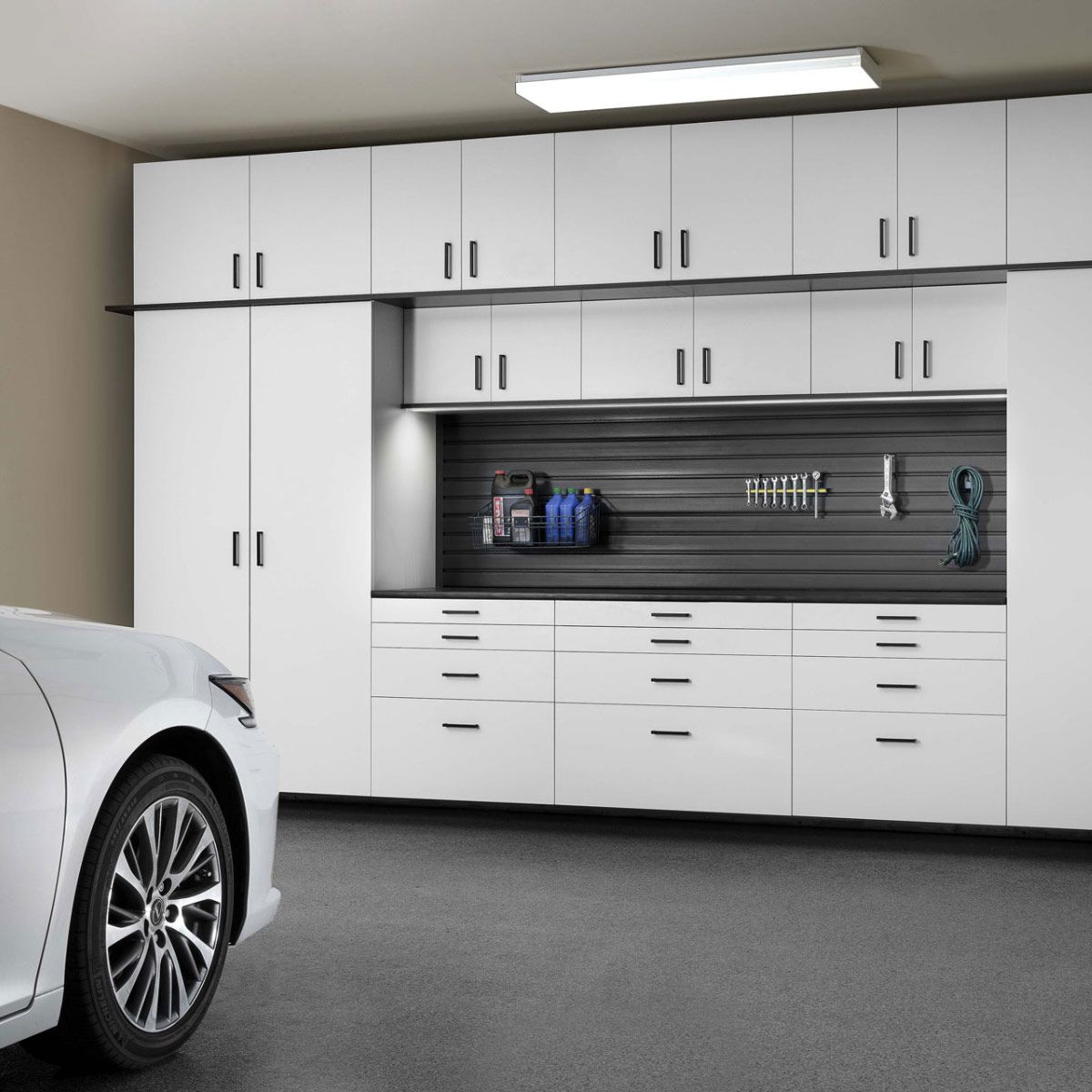 A white car is parked in a garage with white cabinets.