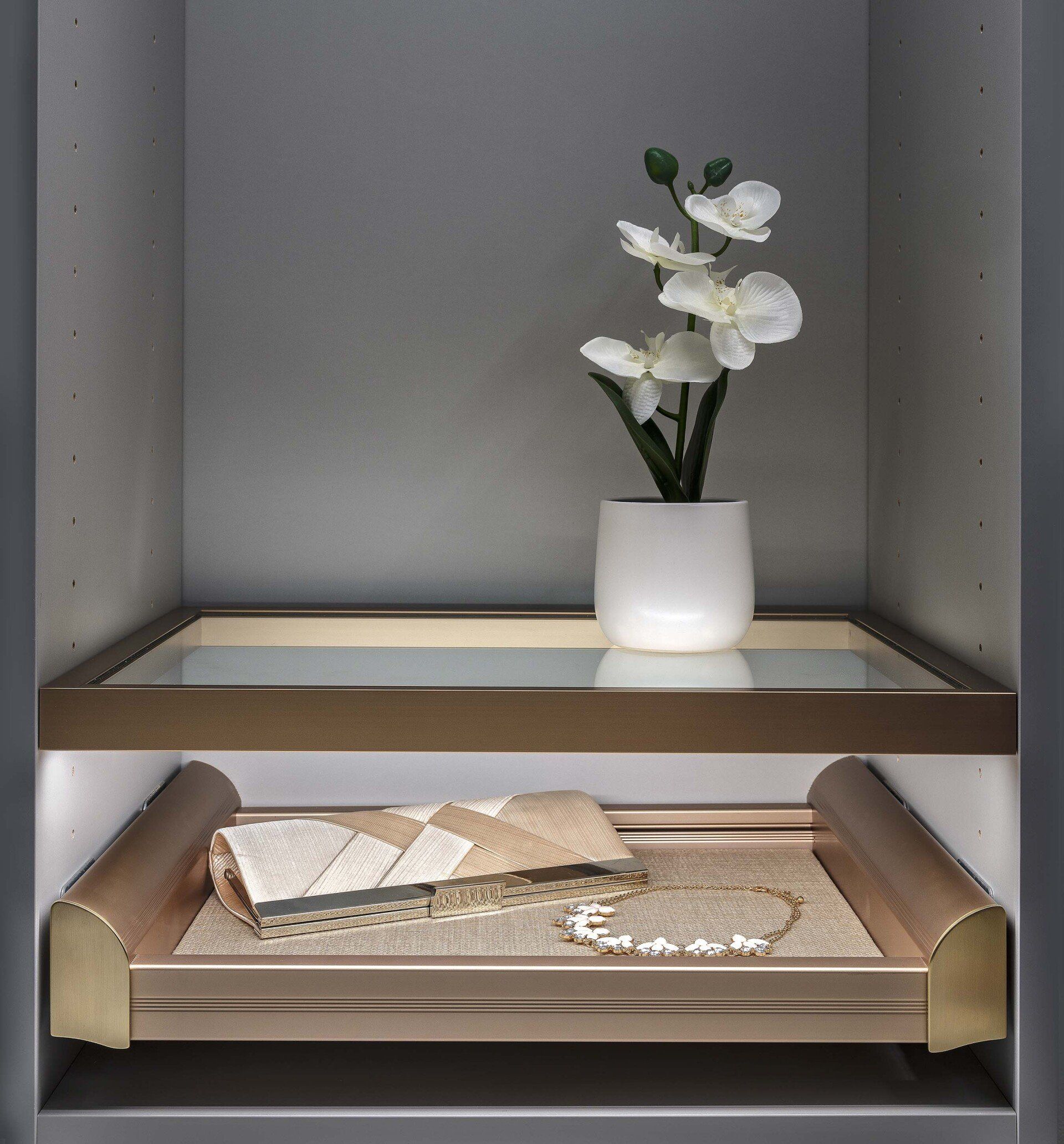 White flowers in a vase on a shelf above a folded cloth in a gray cabinet.