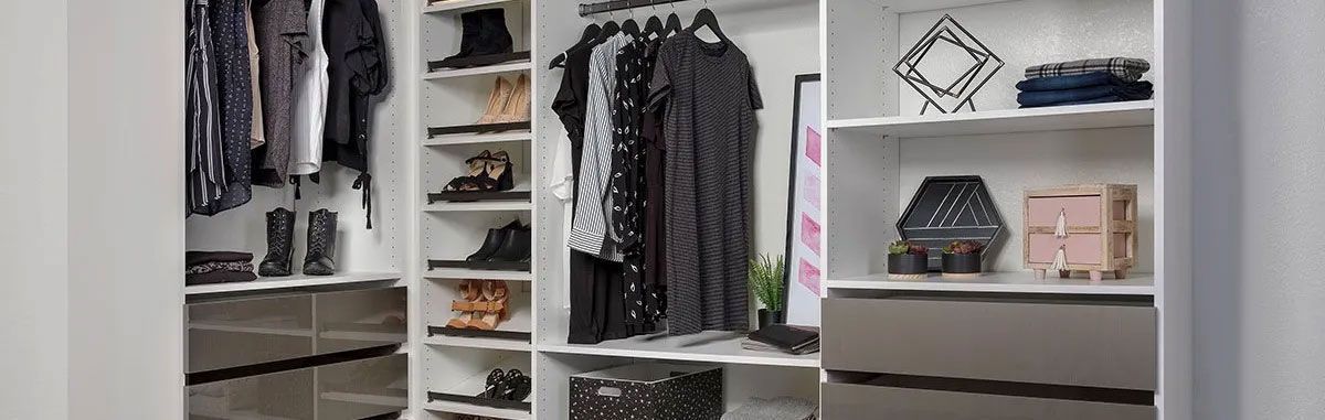 A walk in closet with a mirror and shelves filled with clothes and shoes.