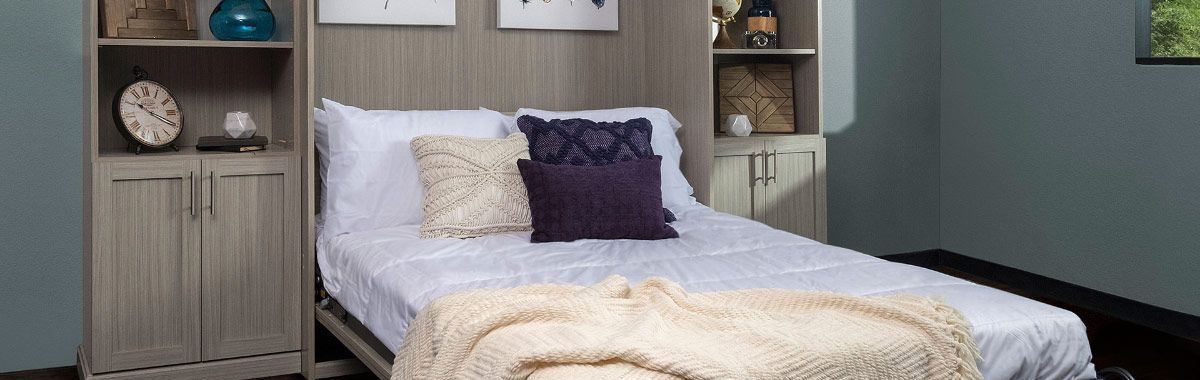 A bed with a blanket and pillows is sitting in a room next to a bookshelf.