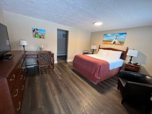 A hotel room with a king size bed , desk , chair and television.