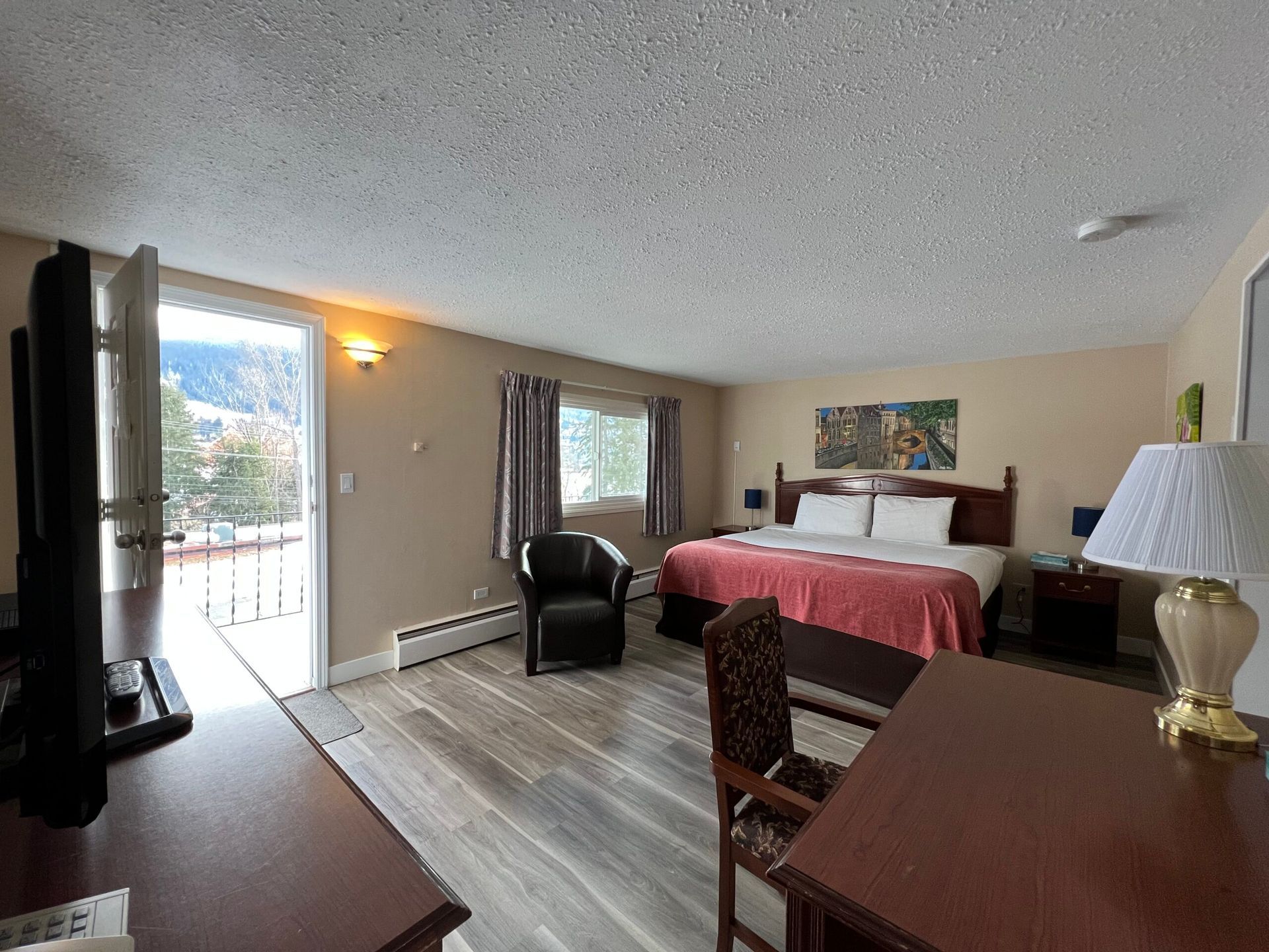 A hotel room with a king size bed , chair , desk and television.