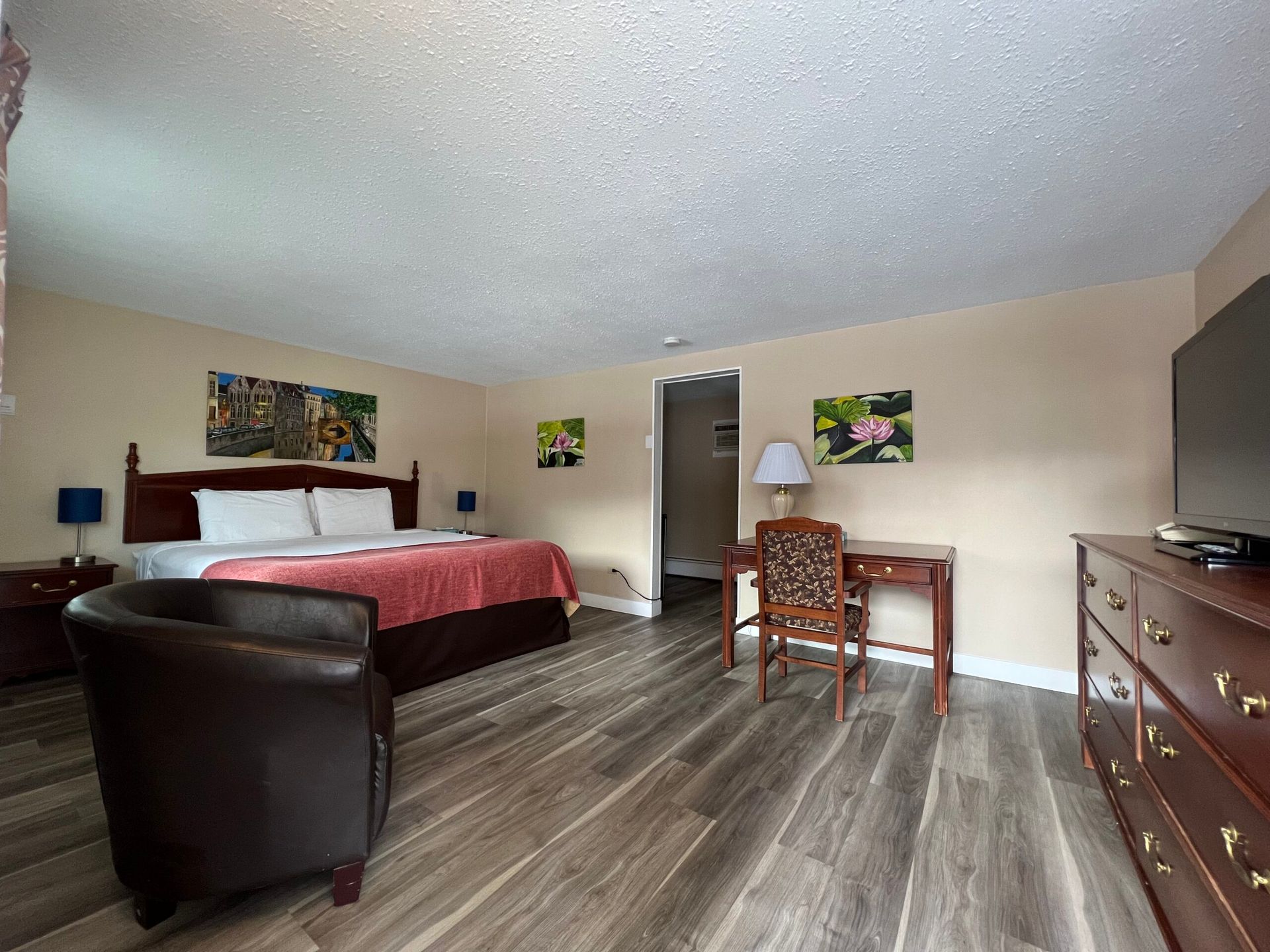 A hotel room with a king size bed , chair , desk and television.
