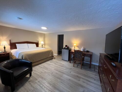 A hotel room with a king size bed , desk , chair and television.