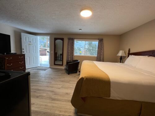 A hotel room with a king size bed , television , dresser and chair.