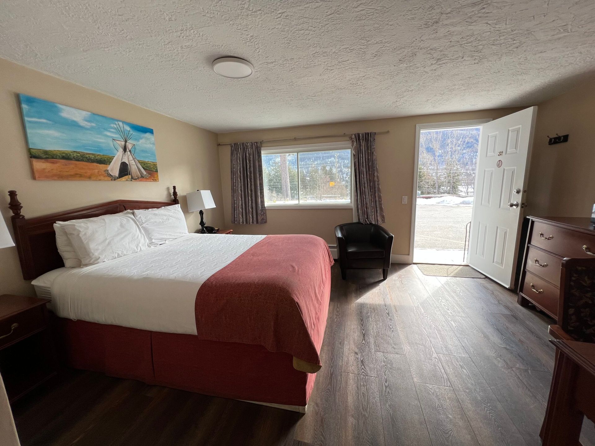 A hotel room with a king size bed , dresser , chair and window.