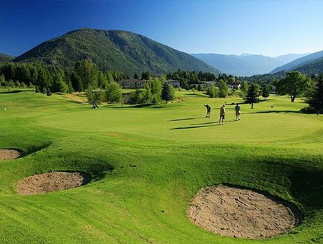 A group of people are playing golf on a golf course with mountains in the background.