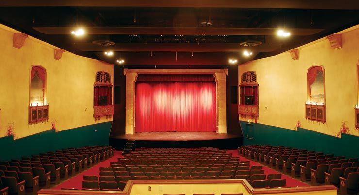 An empty auditorium with rows of seats and a red curtain on the stage.