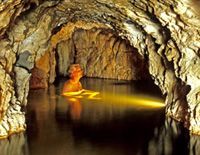 A person is swimming in a cave with a flashlight.