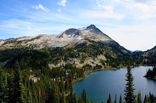 A lake in the middle of a forest with mountains in the background