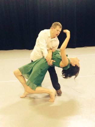 A man in a white shirt is holding a woman in a green dress on a dance floor.