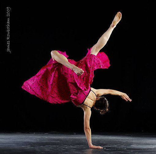 A woman in a pink dress is doing a handstand on a black background