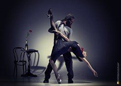 A man and a woman are dancing tango in a dark room.