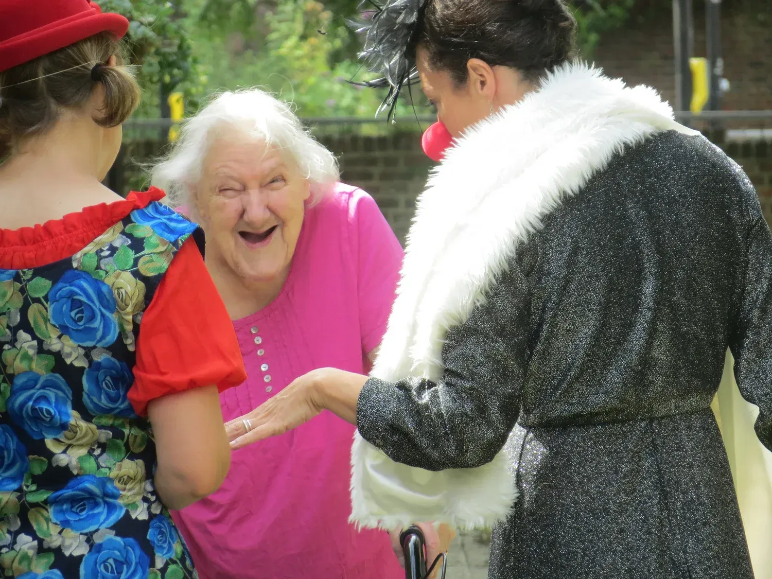 Woman in pink shirt laughs with two people in costume outdoors.