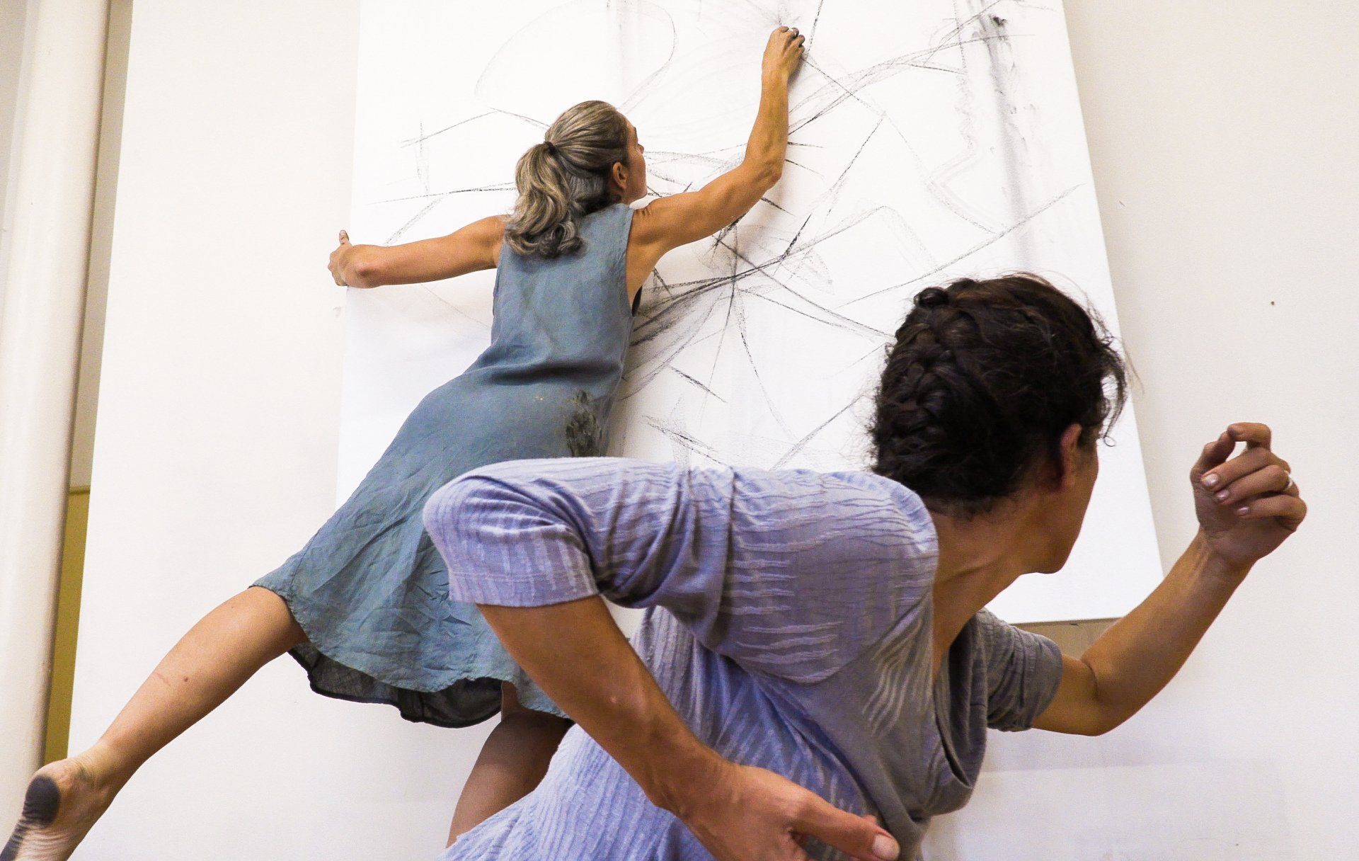 Two women are dancing in front of a white board