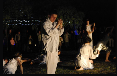 A group of people in white clothes are dancing in the dark