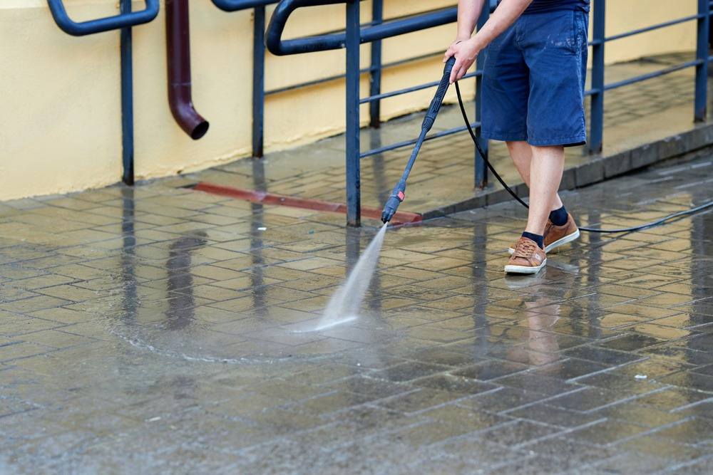 A man is using a high pressure washer to clean a sidewalk.