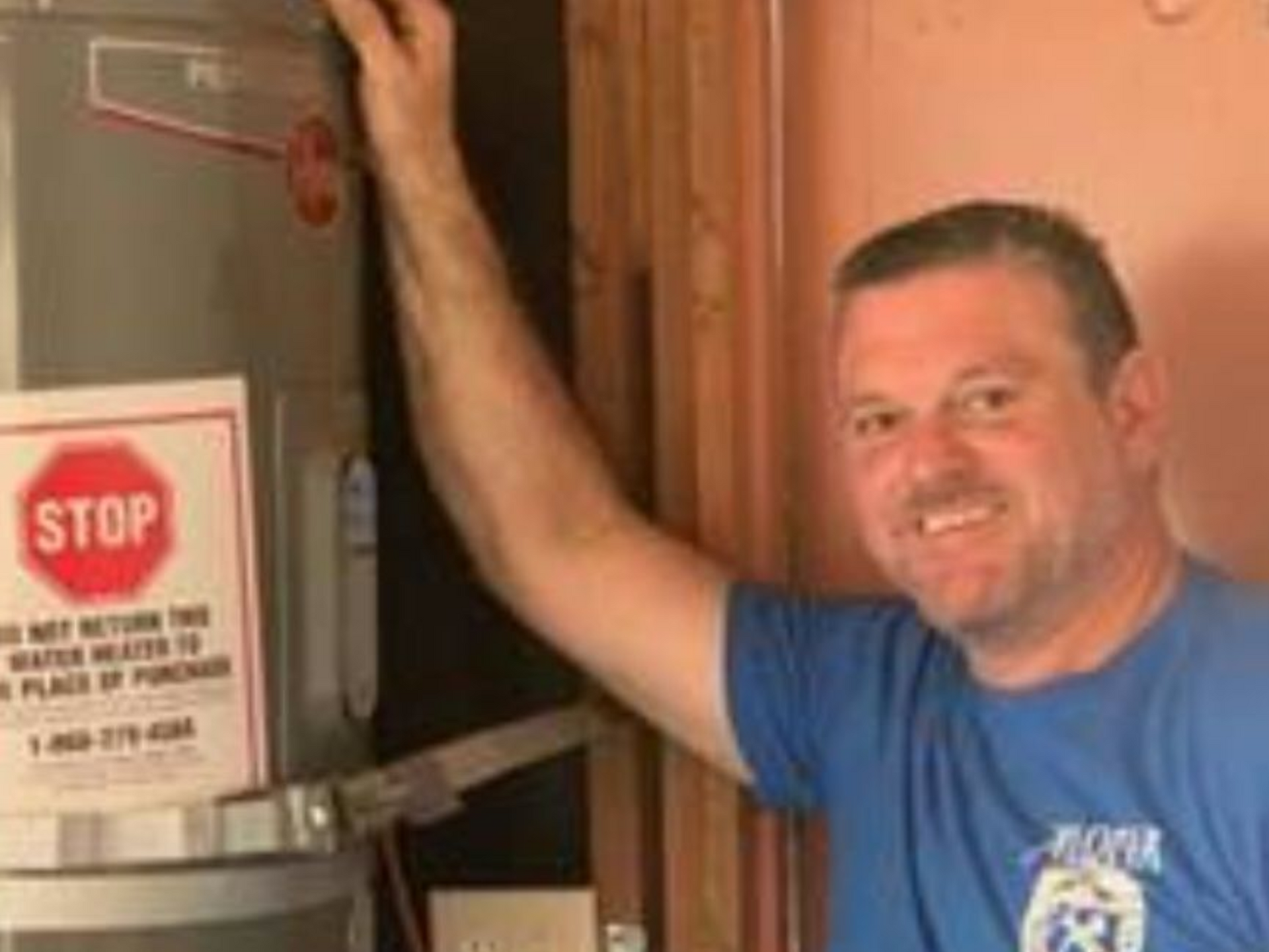 Man smiling beside large metal machine with a red STOP sign in a workshop
