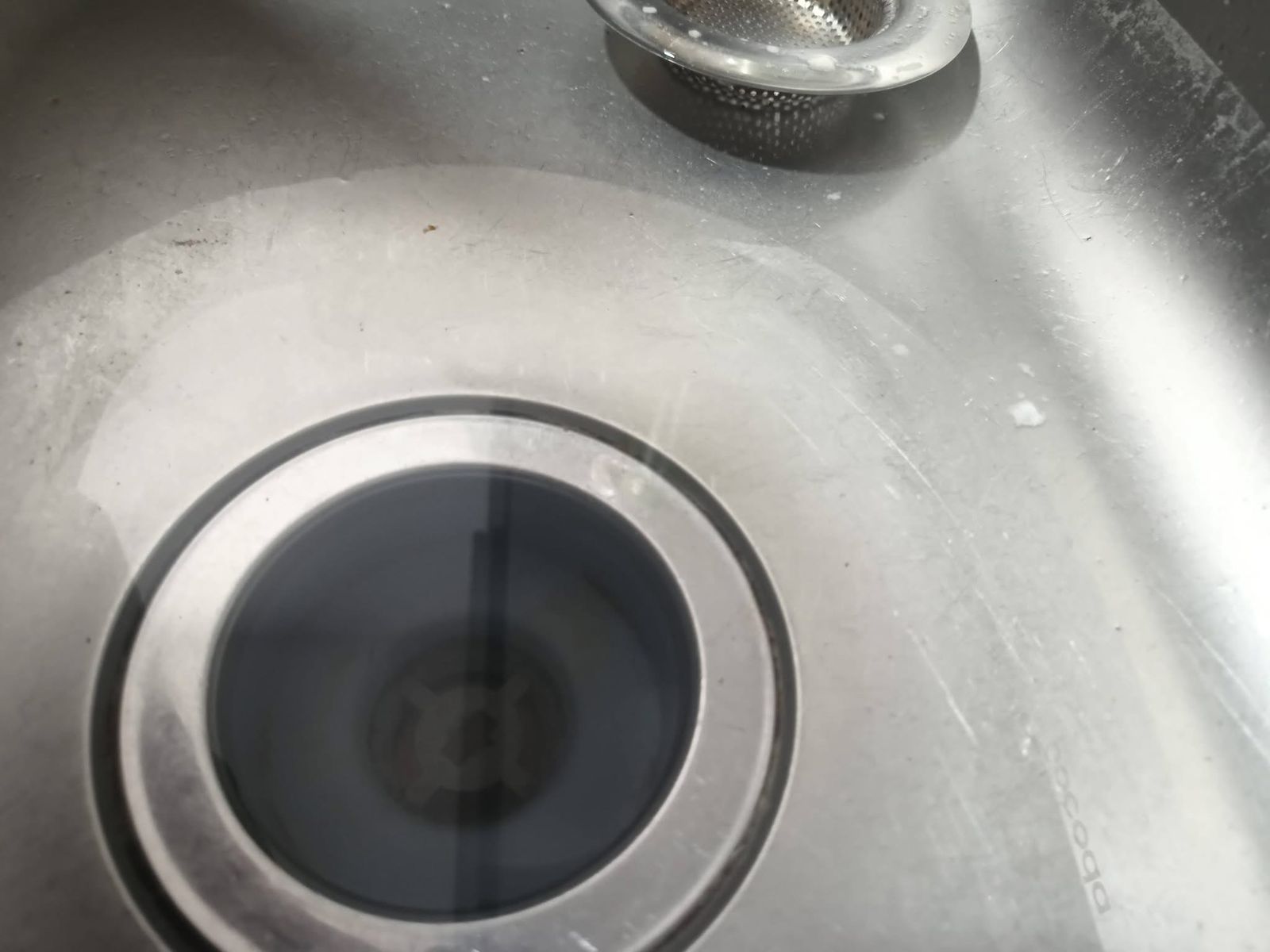 Desagüe de fregadero de acero inoxidable con agua oscura acumulada en el centro.