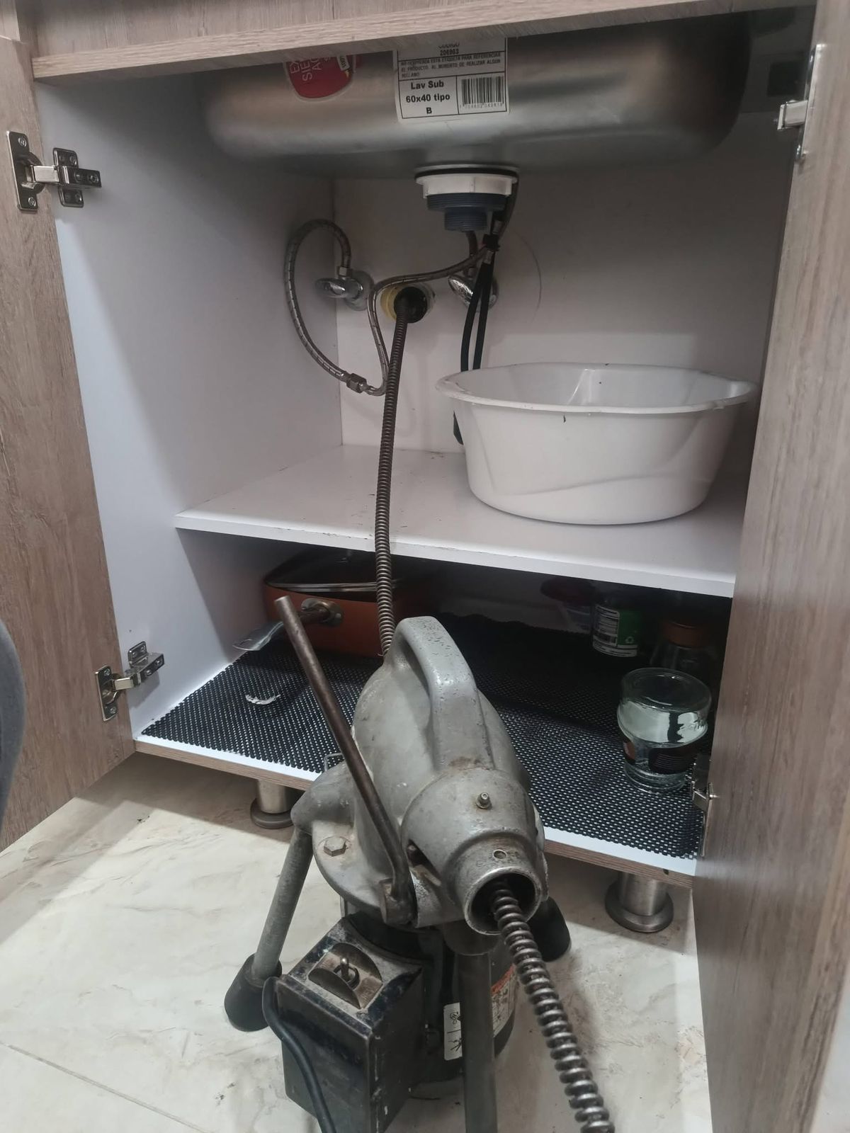 Open bathroom cabinet with plumbing, a white basin, and a hair dryer on the floor.
