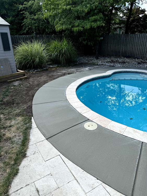 A swimming pool with a concrete deck and a shed in the background.