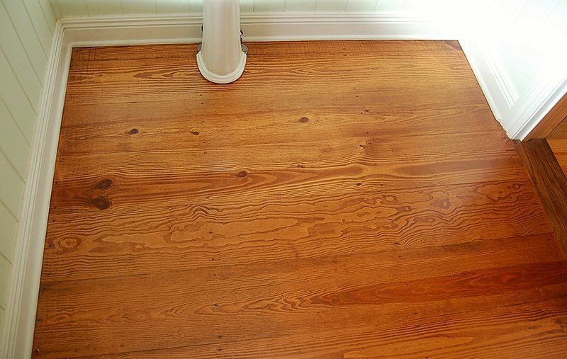 A wooden floor with a white pedestal in the corner of a room.