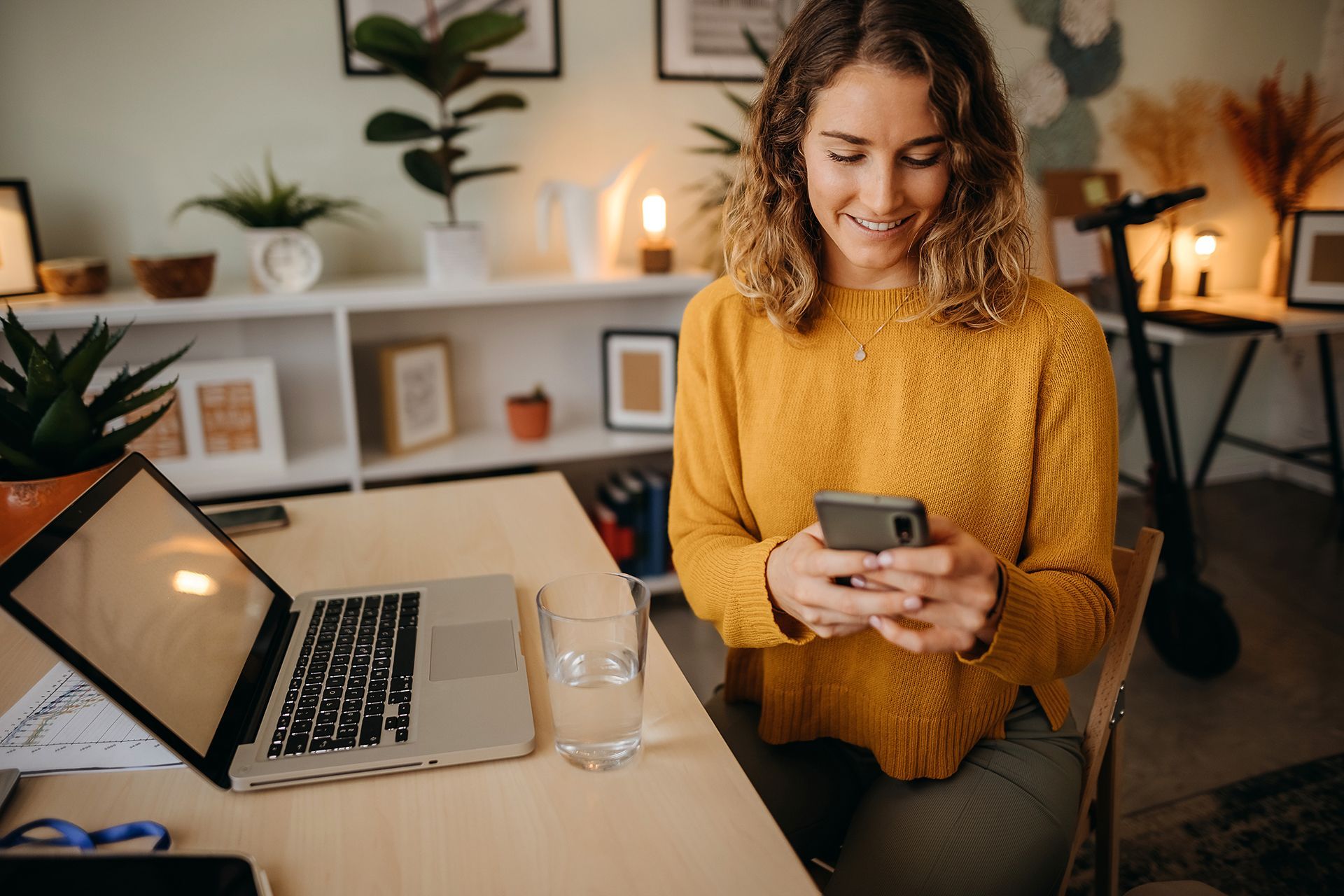 A woman is sitting at a desk looking at her cell phone.