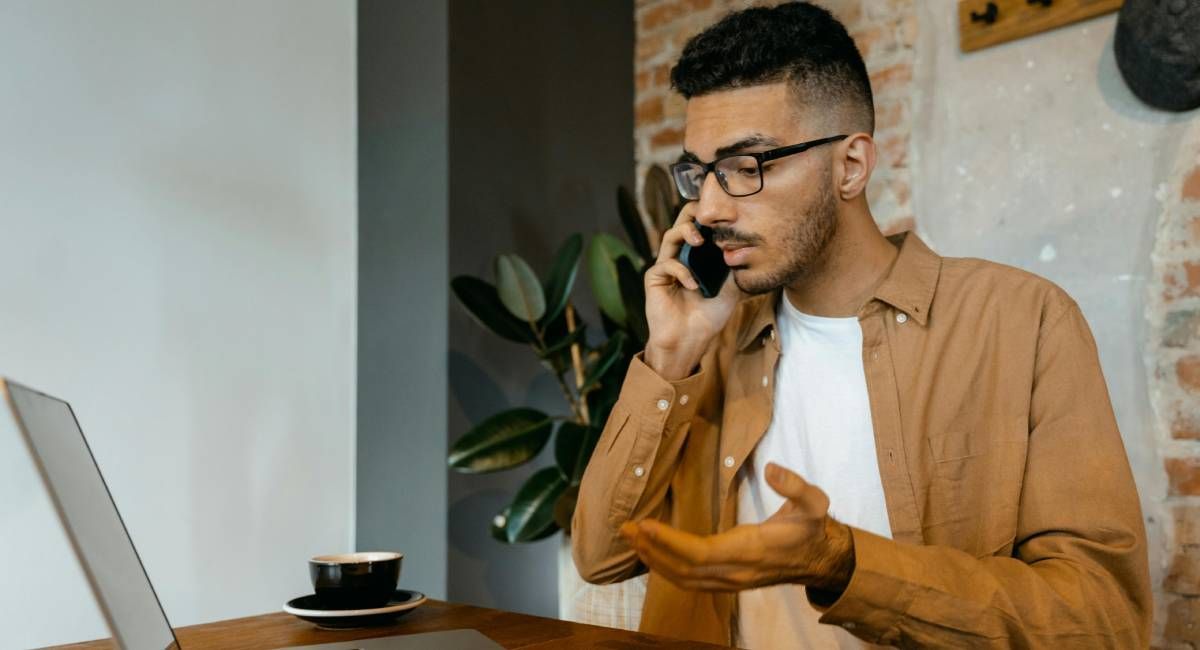 A man looking at a pc confused, and looking for clarification from a colleague over the phone