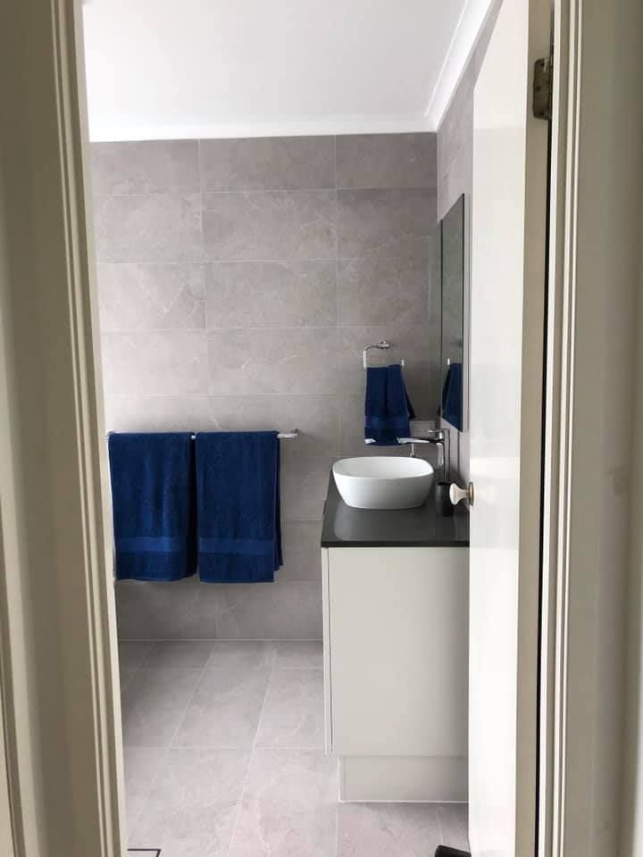Bathroom With Gray Tile Walls and Floor, Vanity With Towels and a Sink — JNR Building And Maintenance in Green Hill, QLD